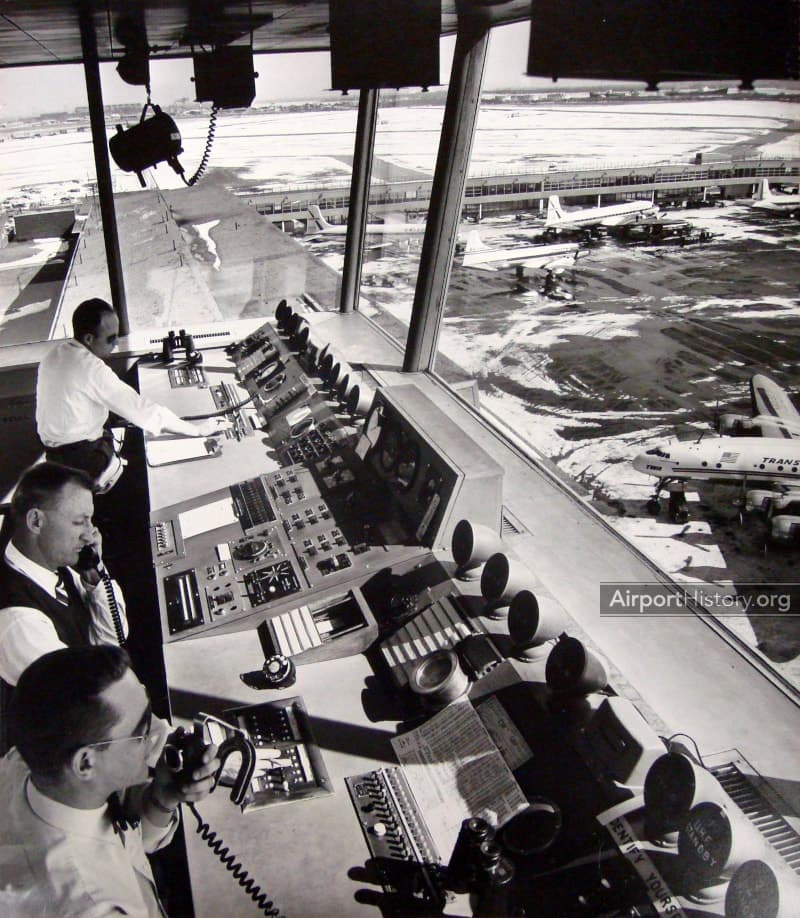 Air traffic controllers working inside a control tower, overlooking aircraft on the tarmac